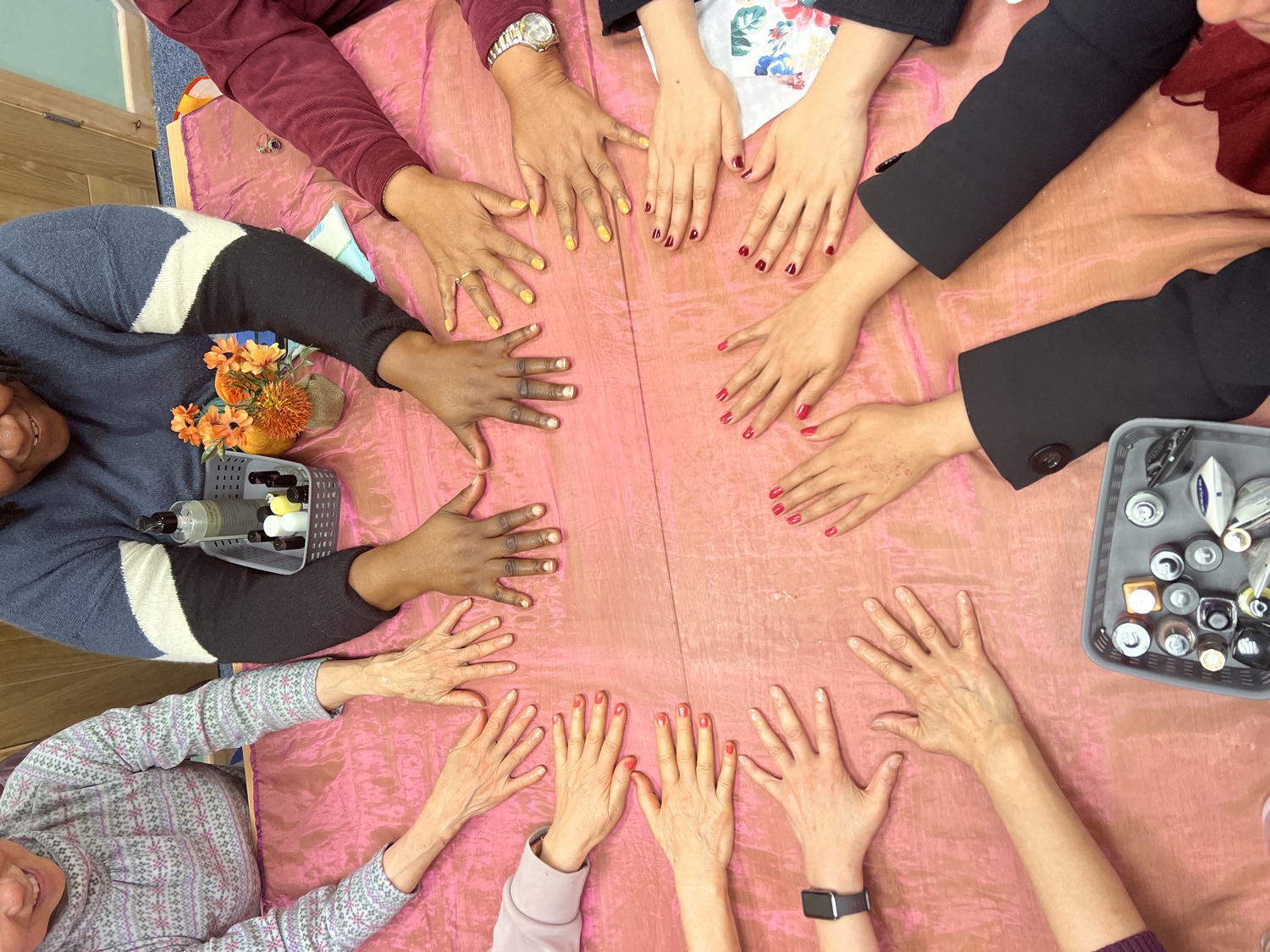 Many hands with freshly painted nails laid in a circle on a pink tablecloth